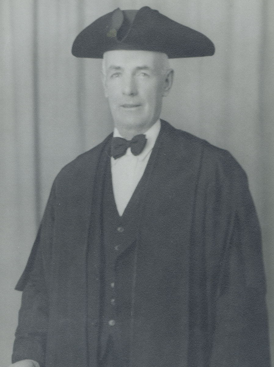 Black and white photo of white male in wardens cap and gown