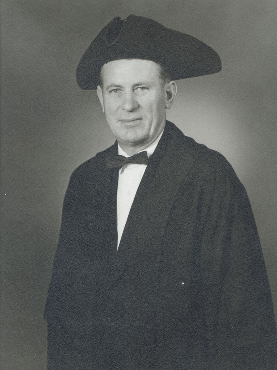 Black and white photo of white male in wardens cap and gown