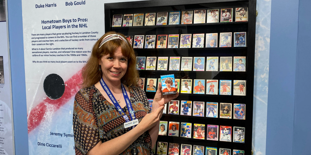 Heritage Museum Curator and Supervisor Dana Thorne holds her personal hockey card in front of a display in the Hockey exhibit