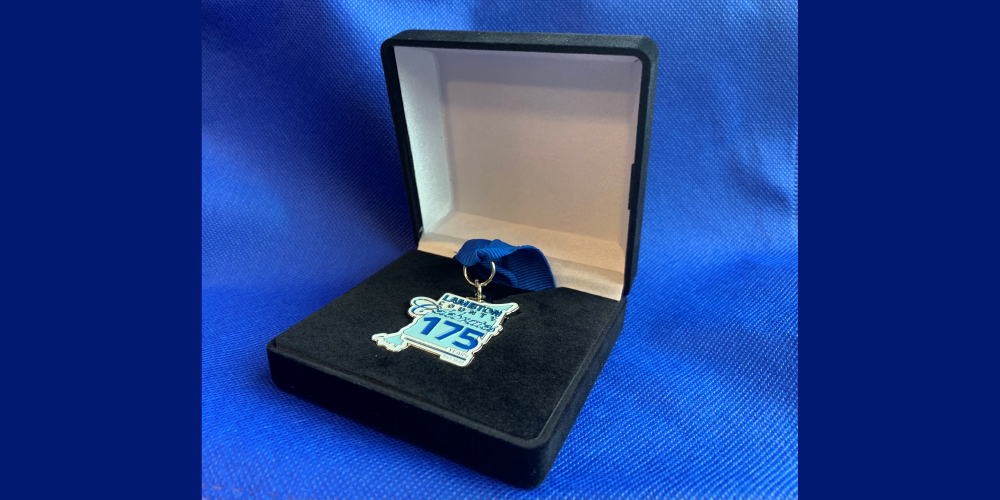Heritage Champions Award medallion in a black box sitting on blue fabric