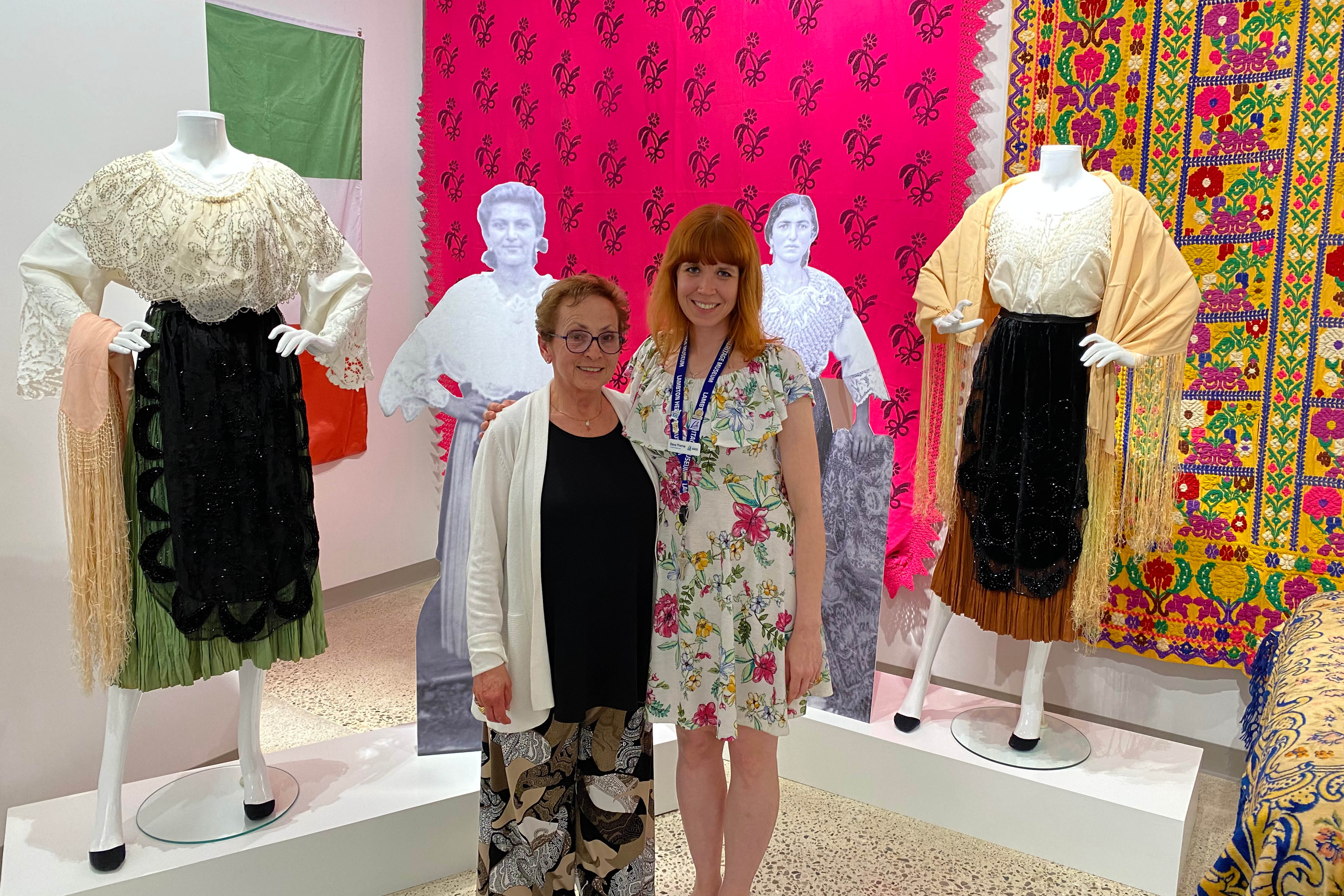 Lambton Heritage Museum Curator/Supervisor Dana Thorne and exhibit contributor Antonia Ambrose stand next to Italian dresses.