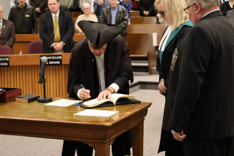 Warden Kevin Marriott signing the Declaration of Office on a table in the centre of Council Chambers